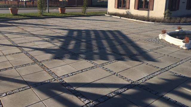 En solbeskinnet gårdsplads med fliser og skygger fra en pergola, der skaber et interessant mønster.
