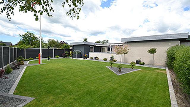 Moderne hus med velplejet græsplæne og dekorative planter i haven under en skyet himmel.