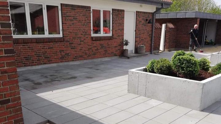 Nyrenoveret terrasse med fliser og planter, en person fejer i baggrunden.
