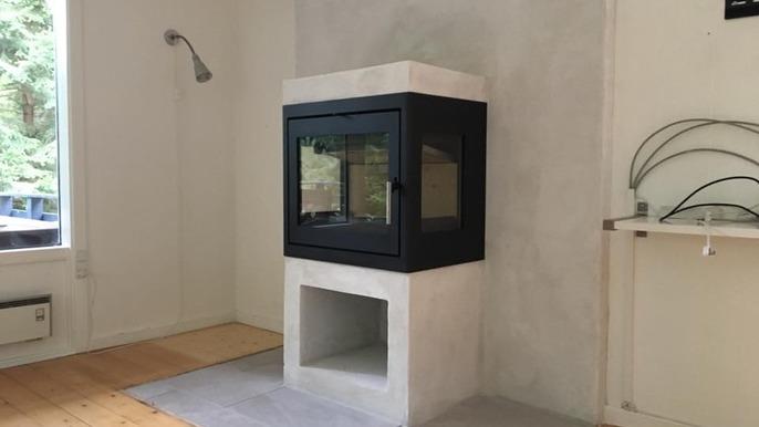 Moderne pejs i stue med beton og sort glas, omgivet af lyse vægge og trægulv.