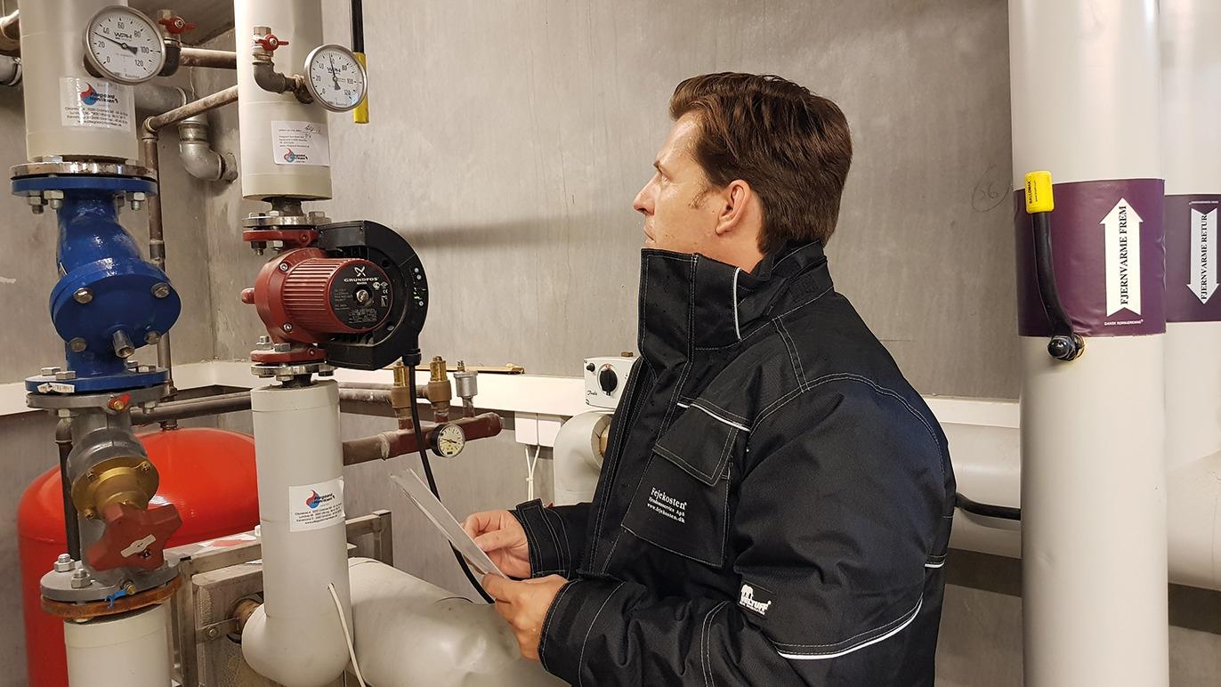 En tekniker inspicerer rør og måleinstrumenter i en industrikælder.