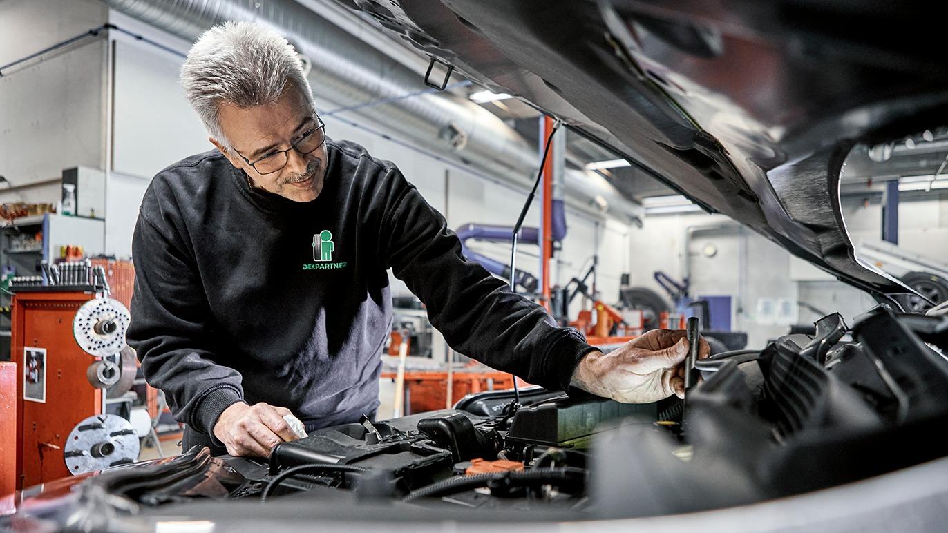 En mekaniker arbejder på en bilmotor i et moderne værksted med værktøj og udstyr i baggrunden.