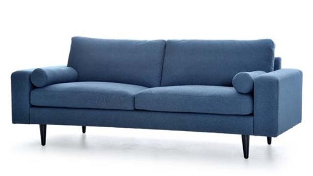 Blå sofa med to puder og runde armlæn, stående på sorte ben.
