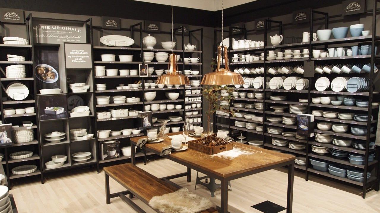 En moderne butik med hylder fyldt med porcelæn og keramik, samt et træbord med kobberlamper.