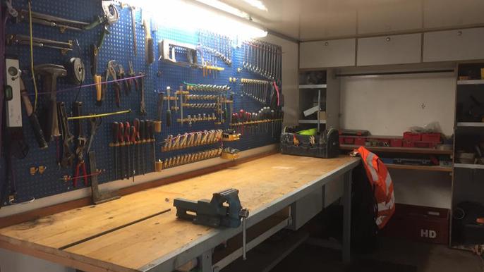 Værksted med værktøjer hængende på væggen og en stor arbejdsbænk i midten.