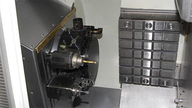 Billede af en CNC-maskine med en roterende værktøjsstation og en metalbearbejdningsplade.