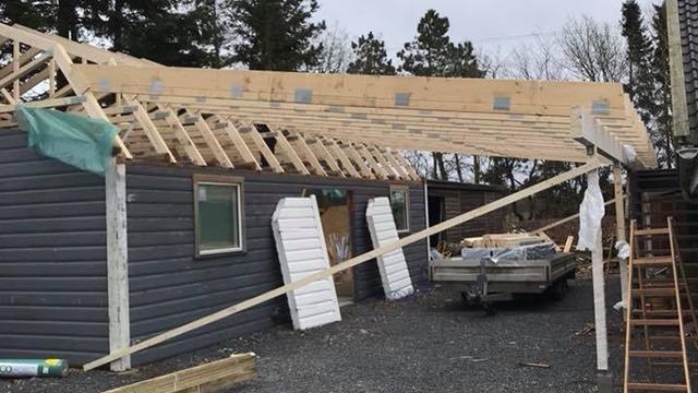 Hus med tagkonstruktion under opbygning, træmaterialer og byggeudstyr synligt i haven.