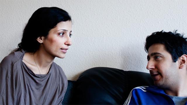 To personer, en mand og en kvinde, sidder på en sofa og taler sammen i et afslappet miljø.