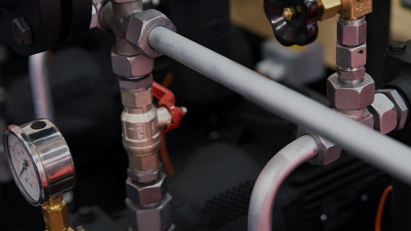 Detalje af rør og fittings på en maskine med trykmåler og ventiler.