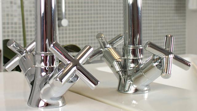 Kromvaskarmatur med krydshåndtag, der reflekterer lys i et moderne badeværelse.