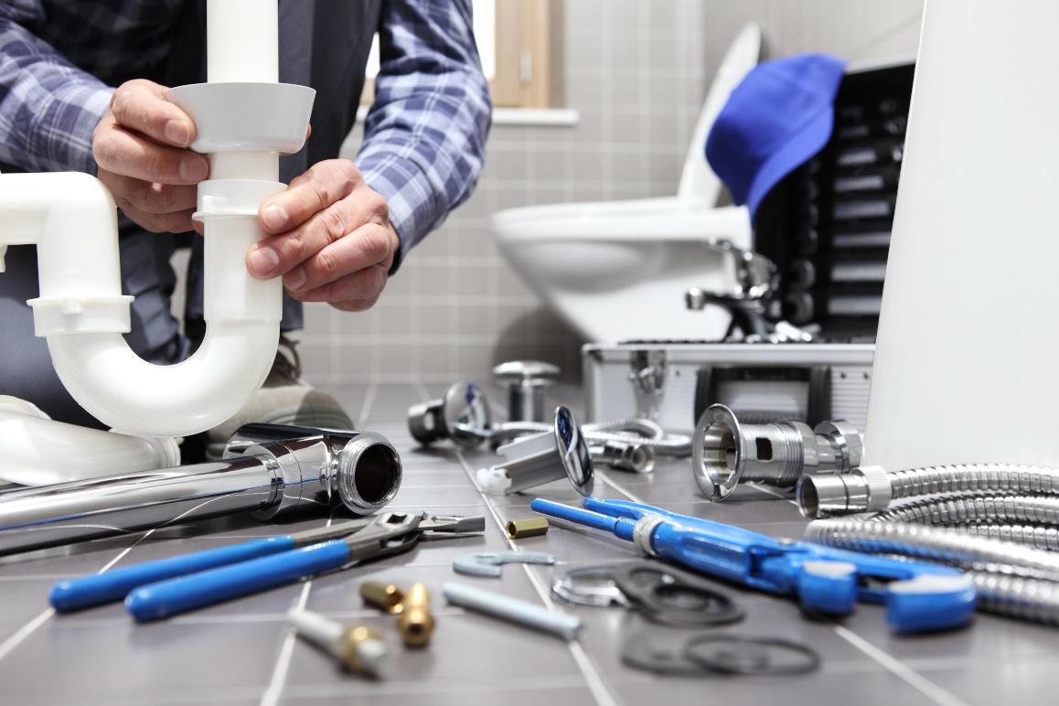En håndværker arbejder med VVS-installationer i et badeværelse med værktøj spredt på gulvet.
