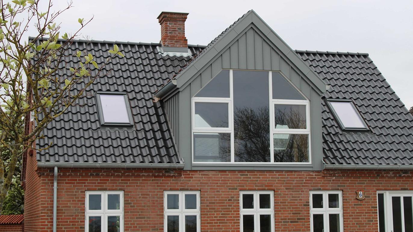 Moderne hus med grå tag og store vinduer i gavlen, beliggende i et roligt kvarter.