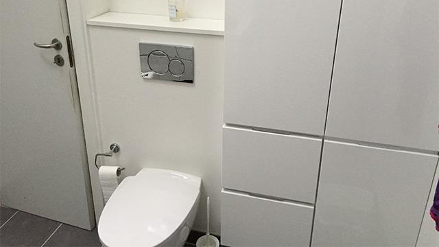 Moderne badeværelse med hvid toilet, skab og toiletpapirholder på grå fliser.