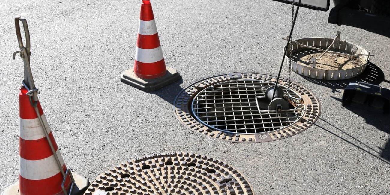 Arbejdsområde med advarselstriangler og åbne brønde på en asfaltvej.