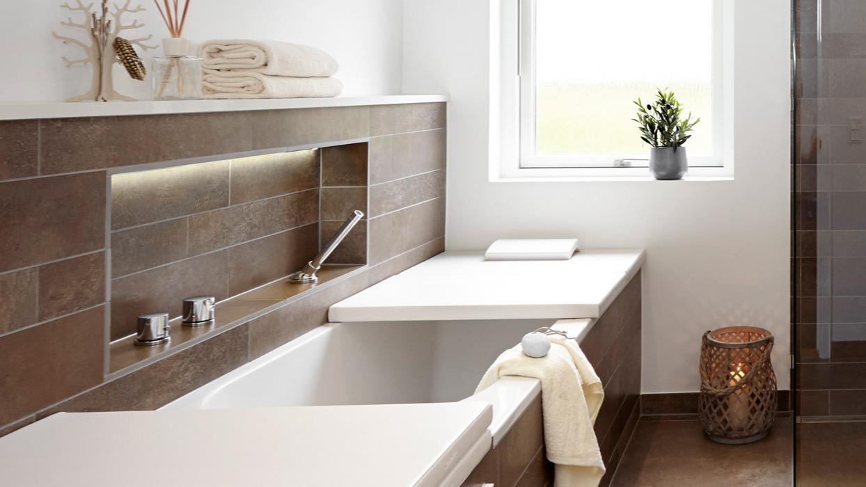 Moderne badeværelse med badekar, håndklæder, planter og stilfuld belysning i brune nuancer.