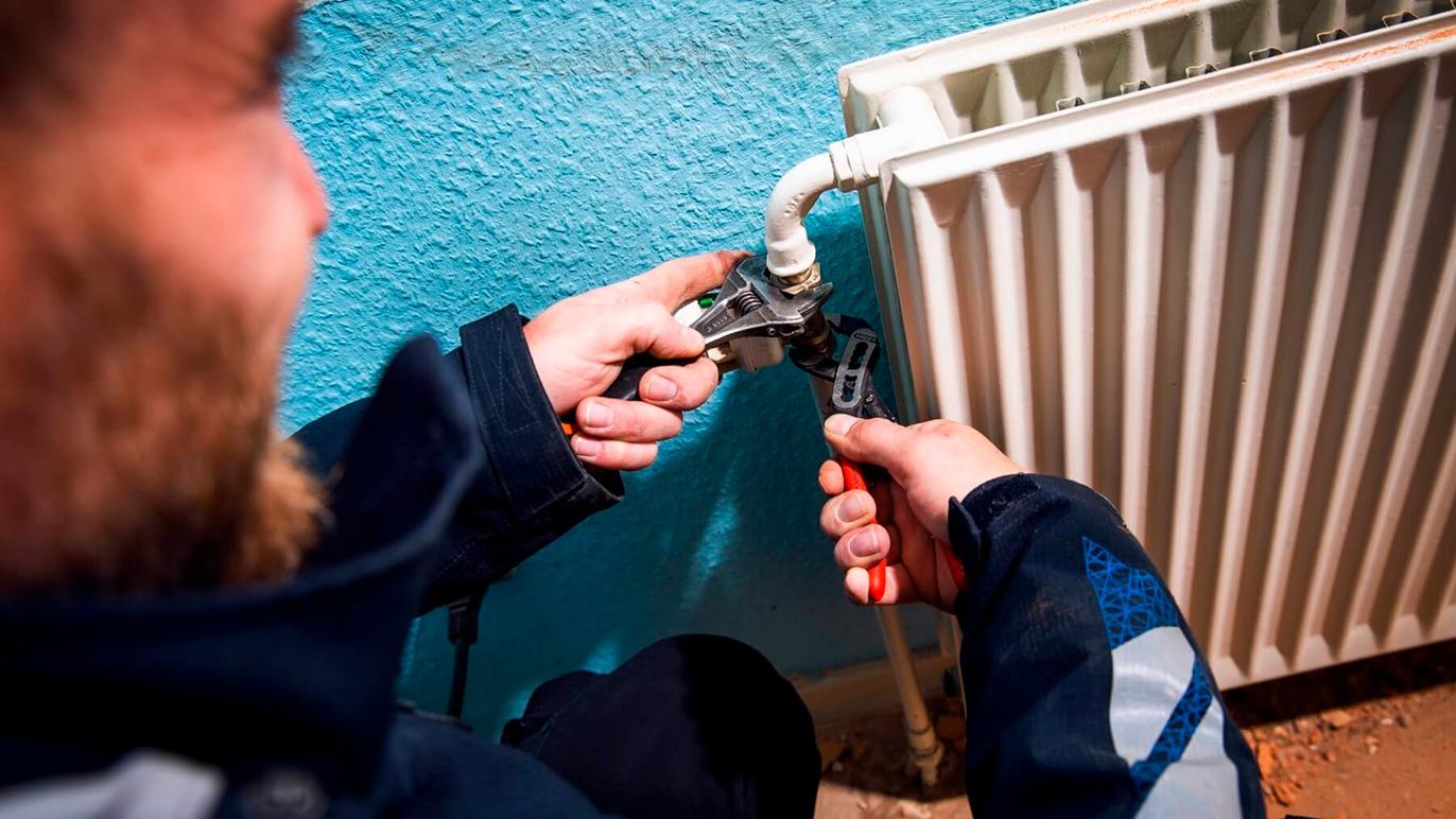 En håndværker arbejder med en radiator og bruger en skruenøgle til at justere rørforbindelsen.