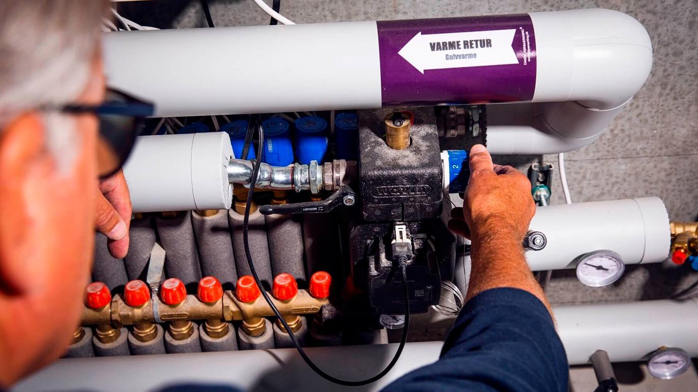 En tekniker justerer rørledninger og ventiler i et varmesystem med synlige måleinstrumenter.
