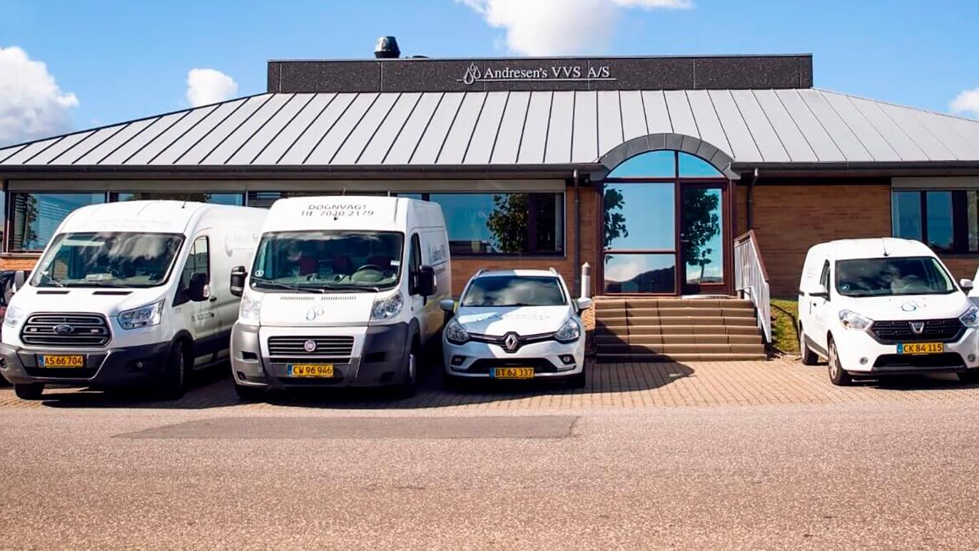 En bygning med en moderne facade og tre varevogne samt en personbil parkeret foran.