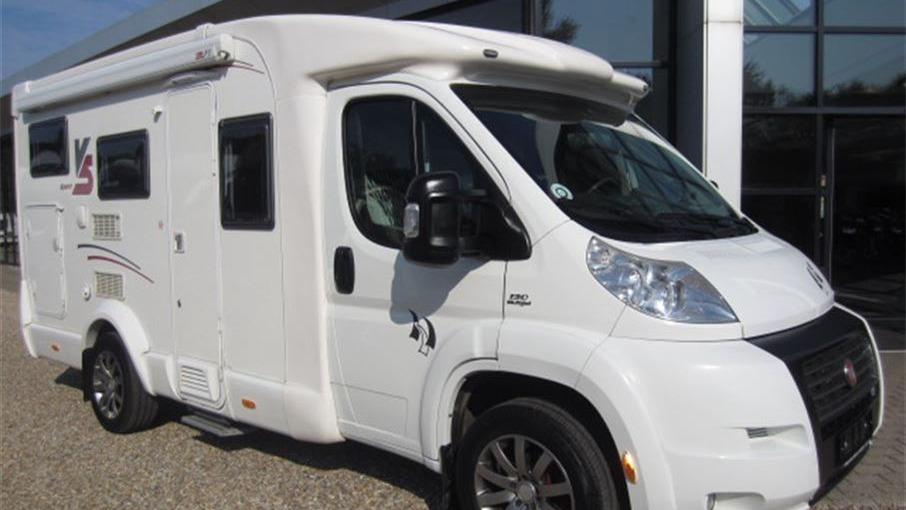 En hvid campingvogn parkeret foran en bygning med store vinduer.