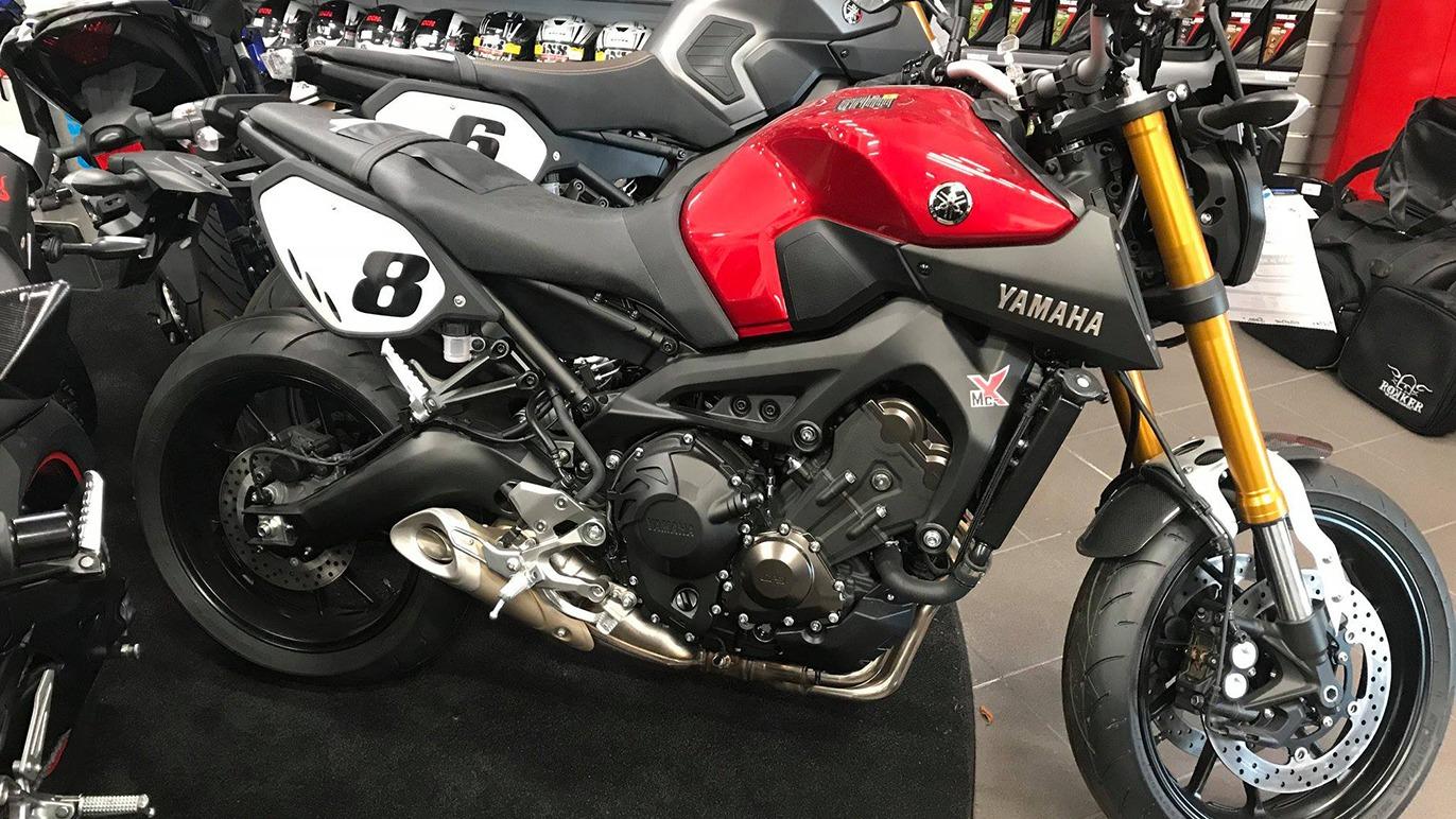 En rød Yamaha motorcykel med sort og sølv detaljer, parkeret blandt andre motorcykler i en butik.