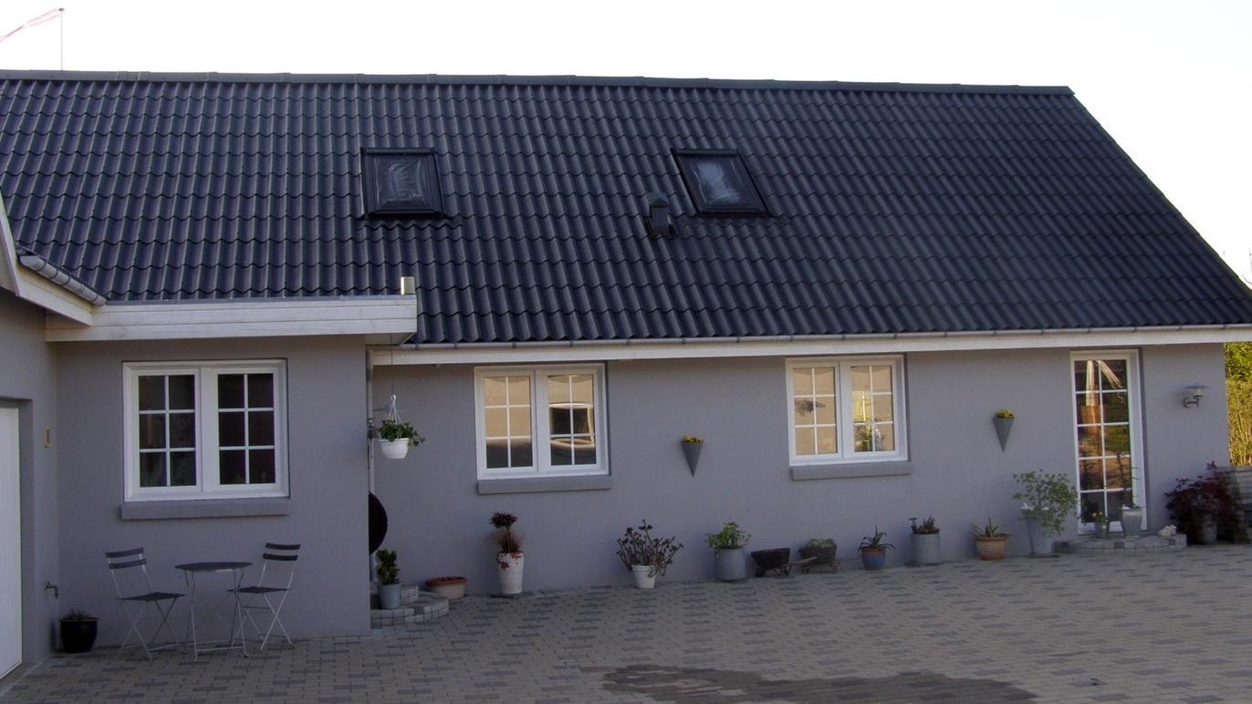Et gråt hus med tag af tegl, vinduer og blomsterkrukker foran indgangen.