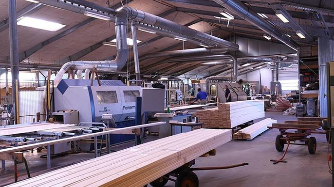 En træbearbejdningsfabrik med maskiner og lange planker, der er klar til forarbejdning.