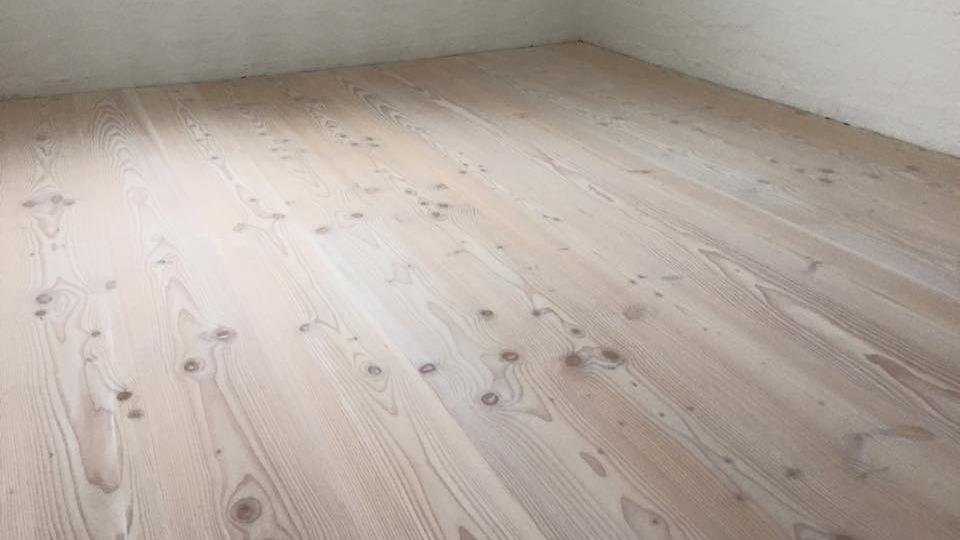 Lyst, ubehandlet trægulv med synlige knaster i et tomt rum.