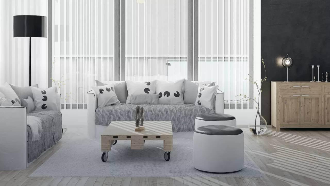 Moderne stue med grå sofaer, dekorative puder, et træbord på hjul og en lys lampe ved vinduet.