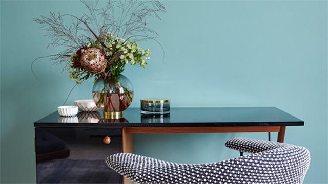 Moderne skrivebord med sort overflade, dekorativ vase med blomster og en komfortabel stol i et stilrent rum.