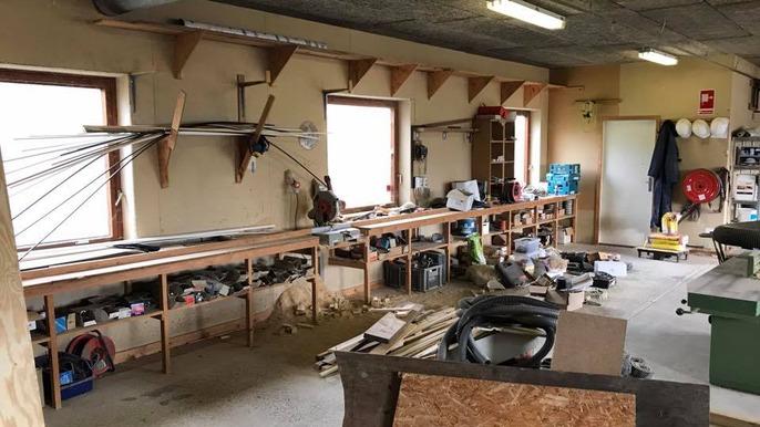 Et værksted med en lang arbejdsbænk, værktøj, materialer og vinduer, der giver naturligt lys.