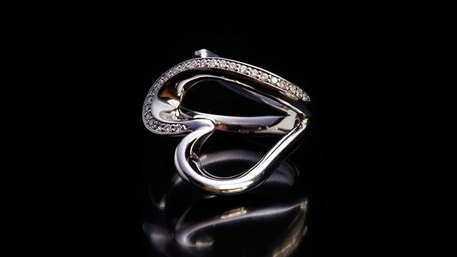 Sølvring med hjerteformet design og glitrende diamanter på en sort baggrund.