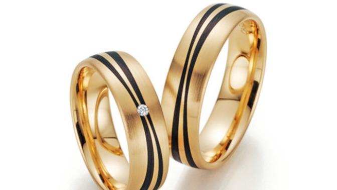 To smukke guld vielsesringe med sorte striber og en diamant på den ene ring.