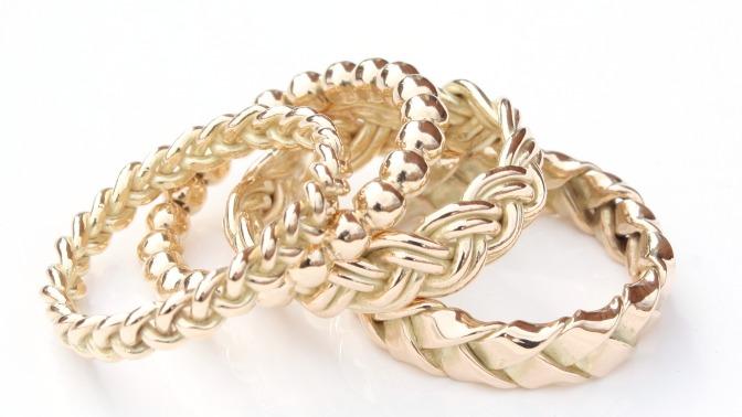 Fire smukke guld ringe med forskellige mønstre og teksturer, herunder flet og perler.