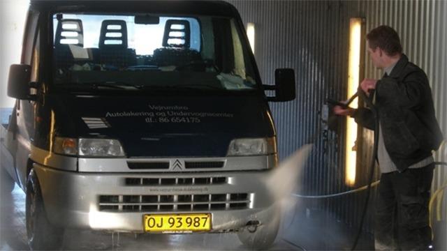 En mand vasker en varevogn med højtryksrenser i en bilvask.