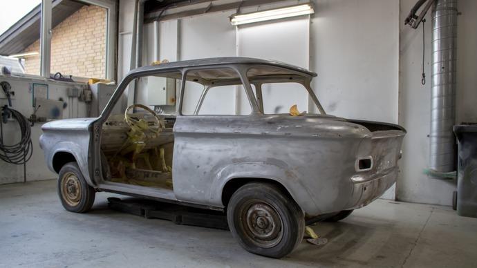 En gammel bil i en garage, delvist adskilt med synlige metaloverflader og rust.