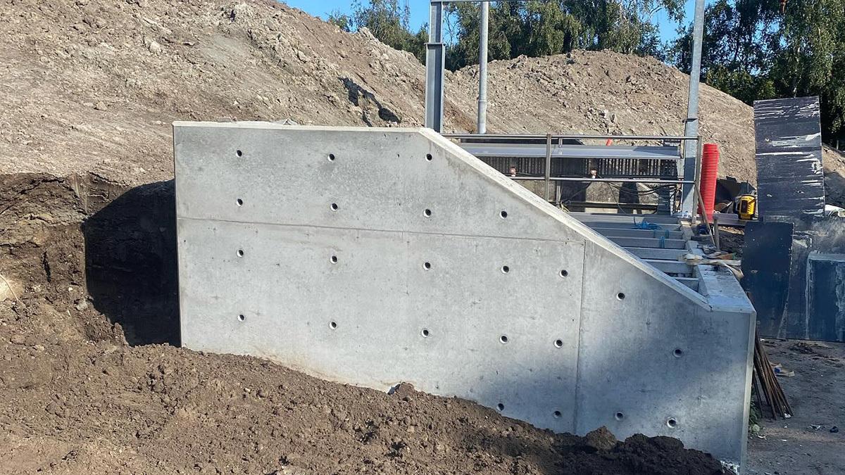 Betonfundament med skråning på byggeplads omgivet af jord og byggeudstyr.