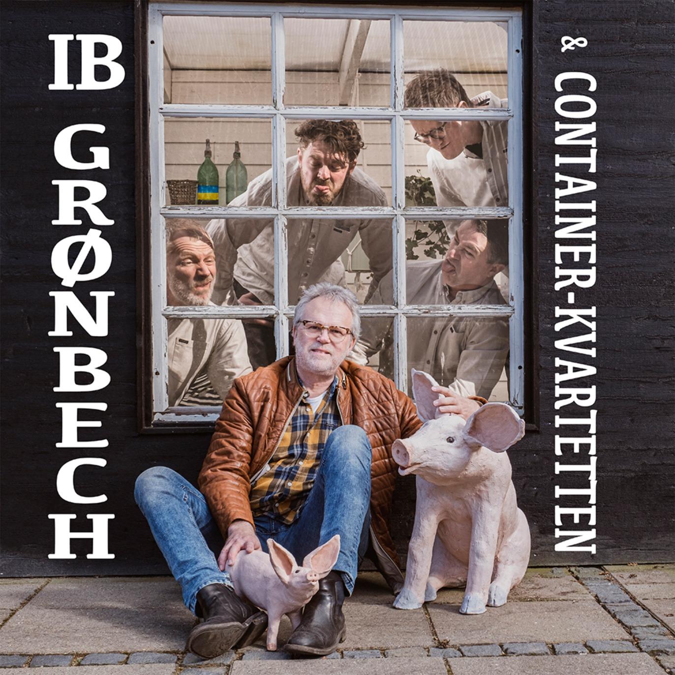 IB Grønbech sidder foran et vindue med Container Kvartetten og to grise, der skaber en festlig atmosfære.