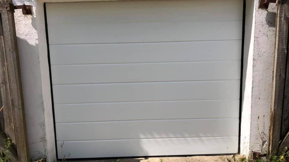 En hvid garageport med lodrette paneler og en græsplæne foran.