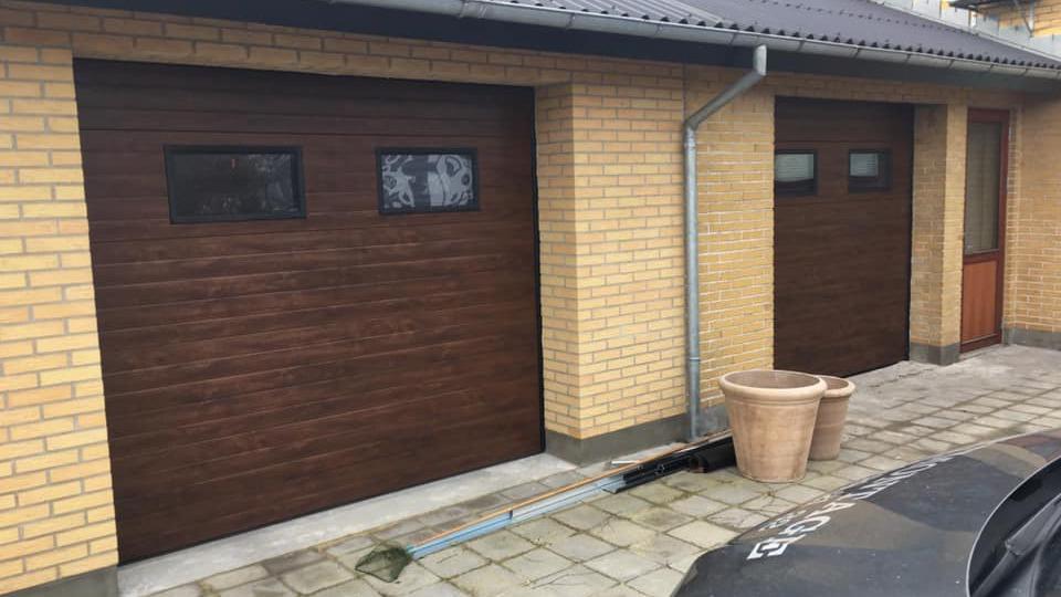 To døre til en garage i trælook med vinduer, beliggende på en murstensvæg.