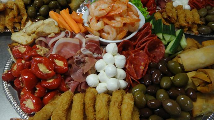 En farverig tapasplatte med rejer, skinke, salami, oliven, fyldte peberfrugter og mozzarella kugler.