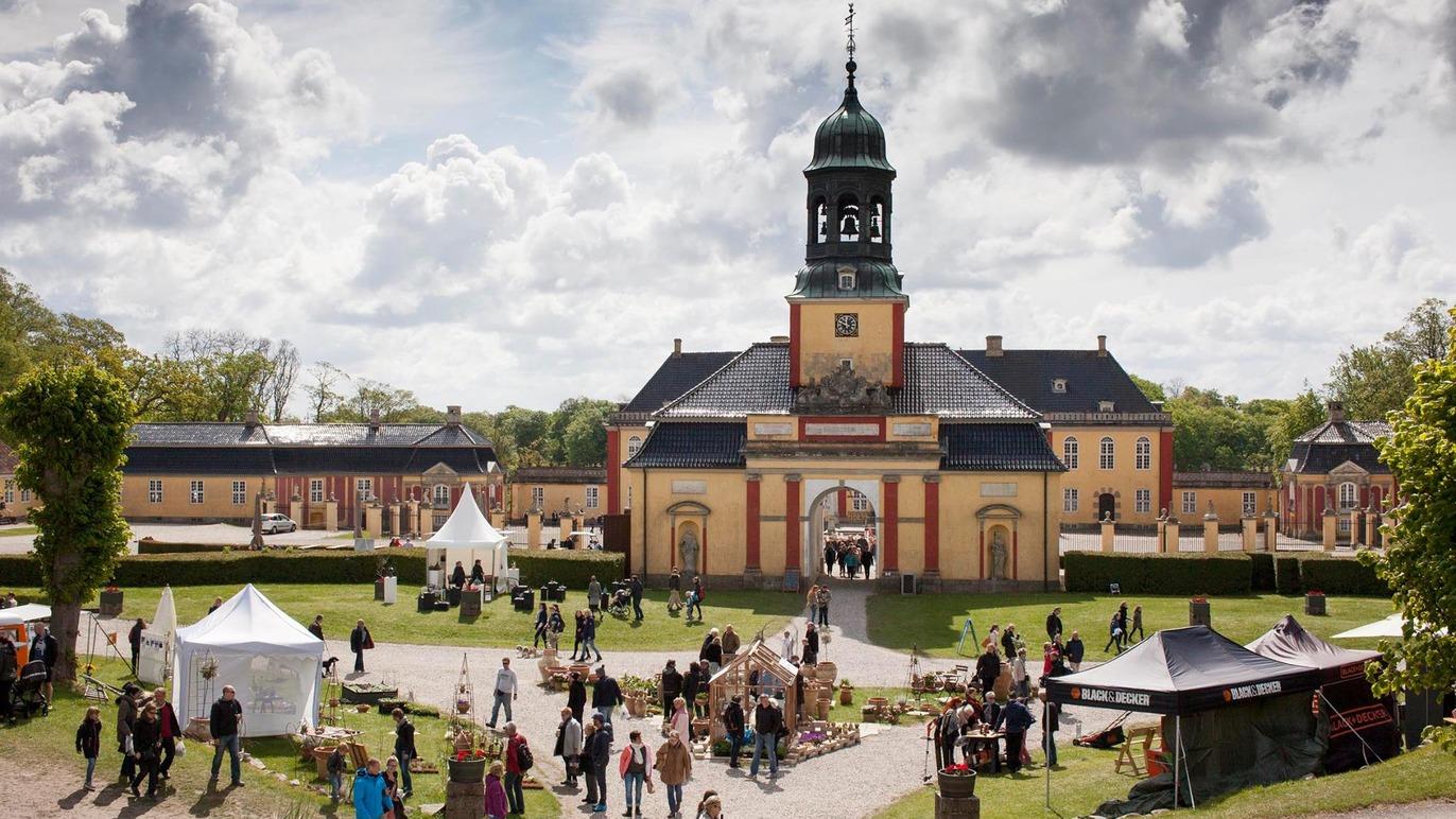 En historisk bygning med klokketårn omgivet af mennesker og boder ved en udendørs festival.
