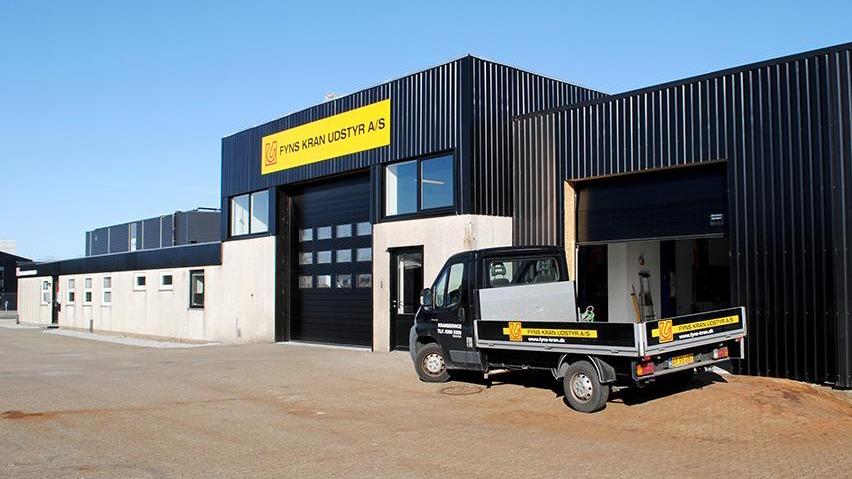 Moderne bygning med sort facade og stor garageport, samt en lastbil parkeret foran.