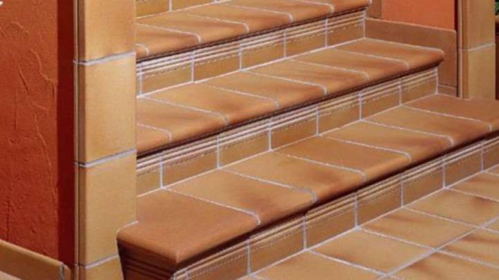 Trappe med fliser i brune og beige nuancer, der fører op til en væg med orange maling.