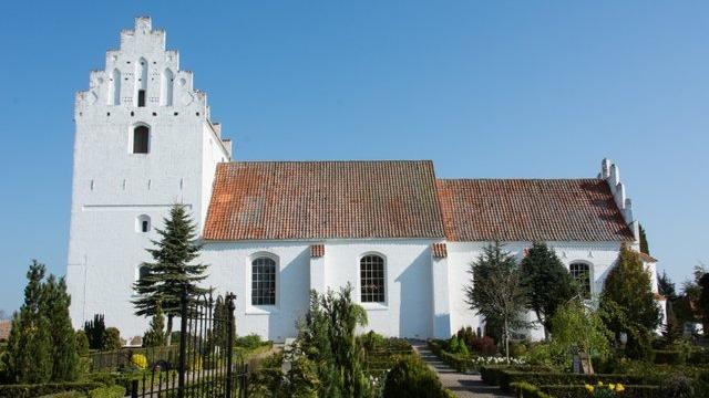 En hvid kirke med en karakteristisk tårn og en smuk have omkring den under en klar blå himmel.