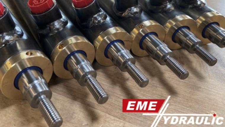 Nærbillede af hydrauliske stænger med metaloverflade og EME Hydraulic-logo i bunden.