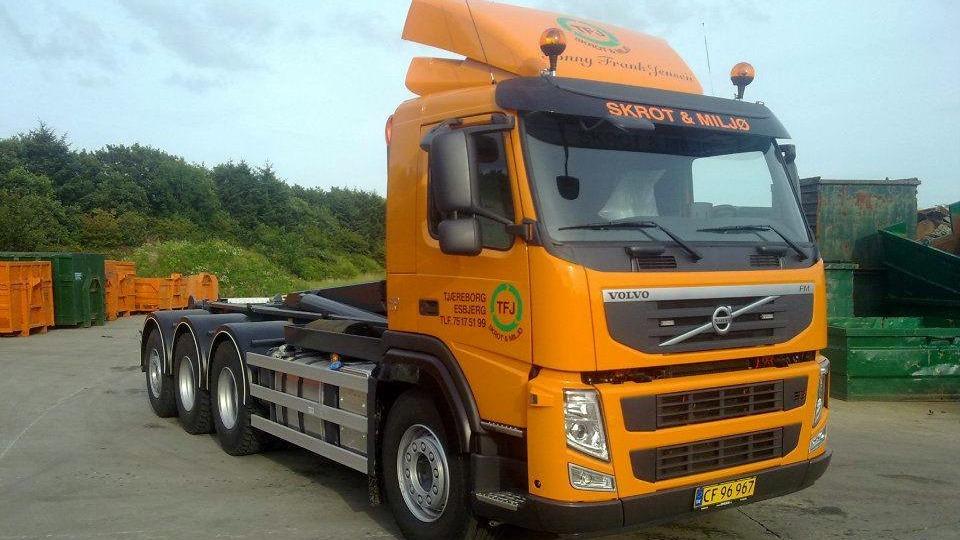 En orange Volvo lastbil parkeret på en byggeplads med affaldscontainere i baggrunden.