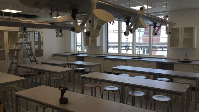 Moderne klasseværelse med borde, stole, og loftventilatorer, samt en stige og værktøj på bordet.