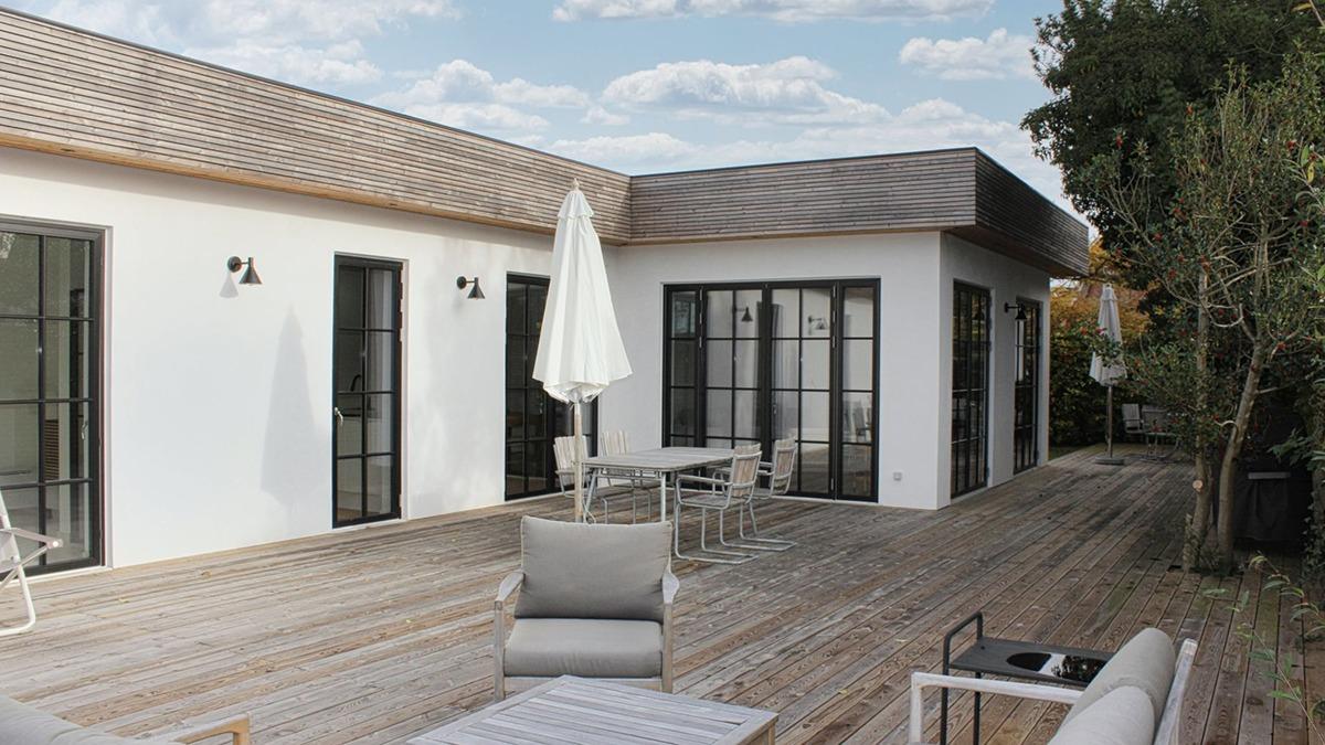 Moderne hus med terrasse, havemøbler og parasol under en skyet himmel.