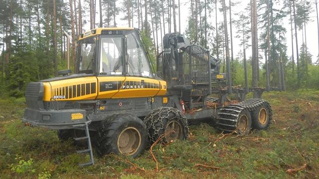 En gult skovmaskine står i en skov med træer og grene omkring den.