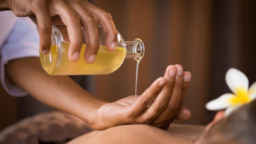 En hånd hælder massageolie fra en flaske over en anden hånd under en afslappende behandling.
